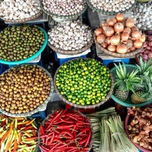 Una vista dall'alto di una bancarella del mercato con cesti di prodotti freschi, tra cui peperoncini, lime, aglio, cipolle e zenzero.