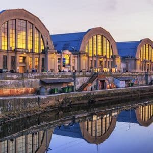 Tres grandes edificios abovedados con ventanas iluminadas en dorado reflejándose en un canal al atardecer.