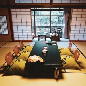A traditional Japanese room with a low table and floor cushions on tatami mats, with shoji screens in the background.