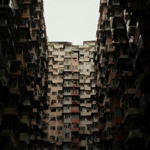 Vista dal basso verso l'alto delle facciate di edifici residenziali fittamente raggruppati sotto un cielo coperto.