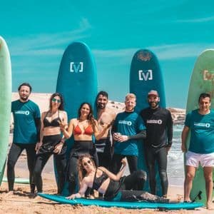 Un gruppo WeRoad di otto persone in muta in posa con le loro tavole da surf su una spiaggia sabbiosa.