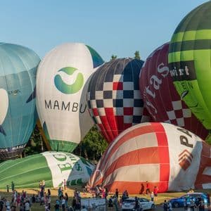 Mongolfiere colorate in varie fasi di gonfiaggio su un campo erboso durante un festival affollato.