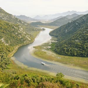Una barca turistica bianca naviga un fiume tortuoso attraverso una valle lussureggiante tra montagne ricoperte di alberi.