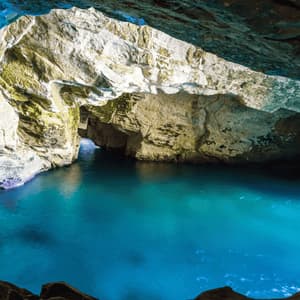Una vista dall'interno di una grotta marina che si apre su acque turchesi, circondata da formazioni rocciose illuminate.