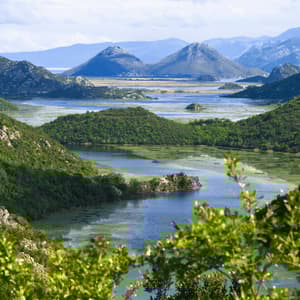 Una vista dall'alto di un fiume che serpeggia attraverso una valle di lussureggianti colline verdi con montagne in lontananza.