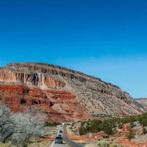 Eine kurvenreiche Straße mit Autos schlängelt sich durch eine Wüstenlandschaft zu einem geschichteten roten Felsplateau.