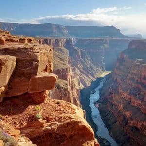 Ein Fluss schlängelt sich durch einen tiefen, weiten Canyon mit geschichteten roten Felsklippen unter einem teilweise bewölkten Himmel.
