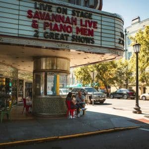 A classic theater entrance with a large marquee advertising 'Savannah Live' on a sunny street corner.