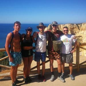 Un groupe WeRoad de cinq personnes posant pour une photo sur un sentier ensoleillé au sommet d'une falaise avec vue sur l'océan.