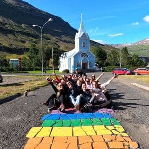 Un grupo de WeRoad posa en un sendero arcoíris, haciéndose una foto frente a una iglesia azul y montañas.