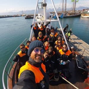 Eine WeRoad-Gruppe in orangen Schwimmwesten posiert für ein Selfie an Deck eines Bootes im Hafen.