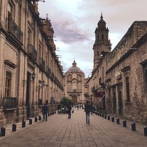 Una vista de una calle peatonal adoquinada bordeada de edificios históricos de piedra, con una gran catedral y un campanario al final.