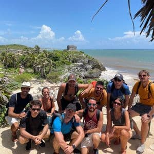 Un viaje en grupo de WeRoad posa para una foto en un acantilado costero con ruinas antiguas y el océano de fondo.