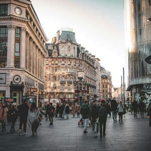 Una folla di persone passeggia lungo un'ampia via pedonale lastricata, fiancheggiata da edifici storici e moderni in città.