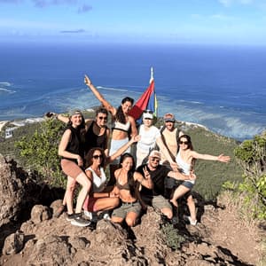 Un voyage de groupe WeRoad posant ensemble sur un sommet de montagne avec une vue panoramique sur l'océan bleu et le littoral.