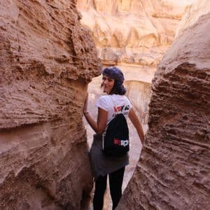Une femme portant un sac à dos WeRoad regarde par-dessus son épaule en marchant dans un canyon étroit en grès.