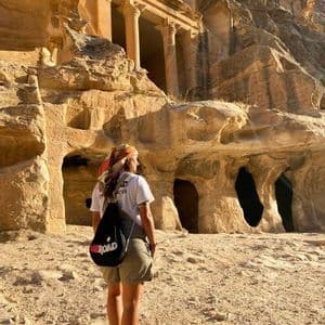 Une personne portant un sac à dos WeRoad se tient devant une ruine antique avec des colonnes sculptées dans une falaise de grès.