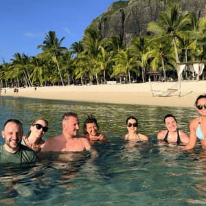 Un groupe WeRoad de sept personnes souriantes dans l'océan, face à une plage tropicale avec des palmiers.