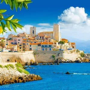 Un borgo costiero fortificato con case colorate si erge su una scogliera a picco sul mare blu, incorniciato da foglie di limoni.