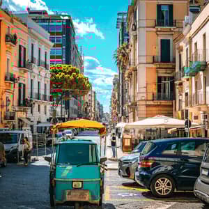 Un veicolo verde a tre ruote parcheggiato su una strada cittadina fiancheggiata da edifici colorati e altre auto sotto un cielo azzurro brillante.