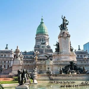 El Palacio del Congreso Nacional Argentino con su cúpula verde, visto desde una plaza con un gran monumento y fuente.