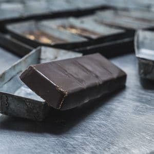 A bar of dark chocolate sits half-removed from its rectangular metal mold on a steel countertop.