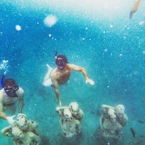 Zwei Männer einer WeRoad Gruppenreise schnorcheln unter Wasser bei versunkenen Statuen.