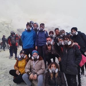 Eine WeRoad Reisegruppe posiert für ein Foto mit Atemschutzmasken in einer rauchigen, vulkanischen Umgebung.