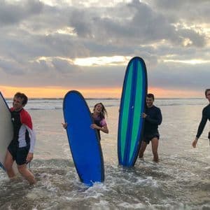 Quattro persone in viaggio di gruppo WeRoad, con tavole da surf, in piedi nell'oceano al tramonto.