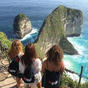 Trois femmes d'un voyage de groupe WeRoad se tiennent sur un sentier à flanc de falaise, observant de grandes formations rocheuses dans un océan turquoise.