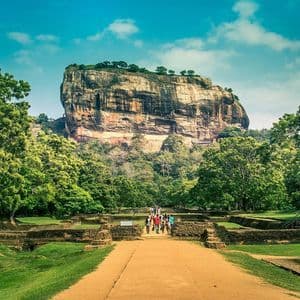 Un grupo de WeRoad recorre un sendero entre ruinas antiguas hacia una gran fortaleza rocosa rodeada de bosque.