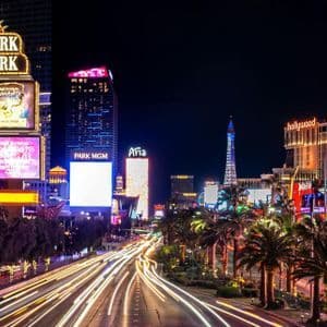 A long-exposure night shot of a busy city street with light trails from cars and bright neon signs on buildings.