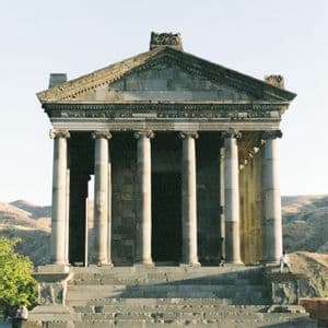 Un temple de pierre avec de grandes colonnes et des marches, dressé sur un fond de collines arides et vallonnées.