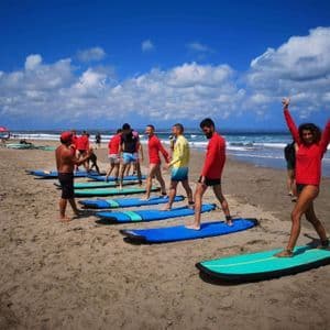 Eine WeRoad-Gruppe nimmt an einem Surfkurs teil und übt auf ihren Boards an einem Sandstrand am Meer.