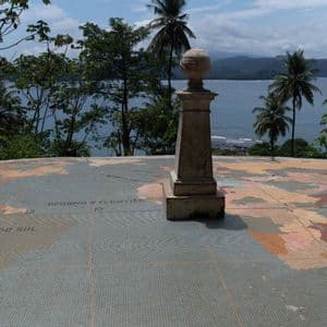 Un monumento in pietra su una grande mappa mondiale a mosaico che mostra l'America del Sud e l'Oceano Atlantico, con vista su una costa tropicale.