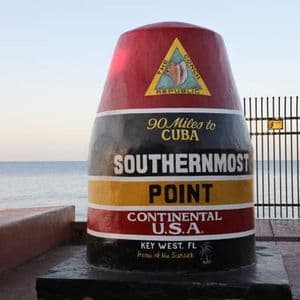The Southernmost Point buoy monument in Key West, Florida, with the ocean visible in the background under a pale sky.