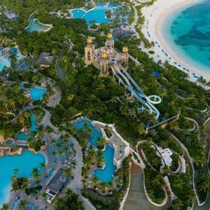 An aerial view of a large tropical resort with pools, water slides, and palm trees next to a white sand beach.