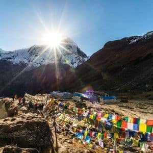 Un voyage de groupe WeRoad sur une crête de montagne ornée de drapeaux de prière colorés, surplombant des sommets enneigés sous un soleil éclatant.