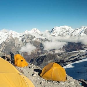 Un grupo de WeRoad acampa en tiendas amarillas brillantes en una ladera rocosa, con una vasta cordillera de picos nevados al fondo.