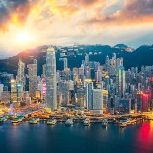Una vista aérea de un denso paisaje urbano con rascacielos iluminados a lo largo de la costa al atardecer.
