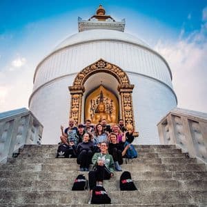 A WeRoad group trip poses for a photo on the steps of a white stupa, with a golden Buddha statue in a niche behind them.
