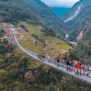 Un gruppo WeRoad saluta da un lungo ponte sospeso, decorato con bandiere colorate, che attraversa una profonda valle con montagne verdi e terrazzate.