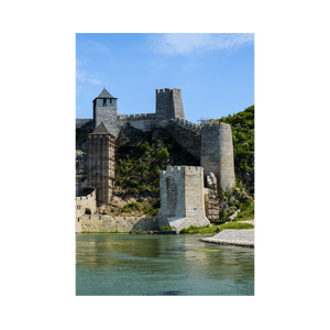 Una fortezza medievale in pietra con più torri si erge su un verde pendio, al margine di un ampio fiume, sotto un cielo blu.