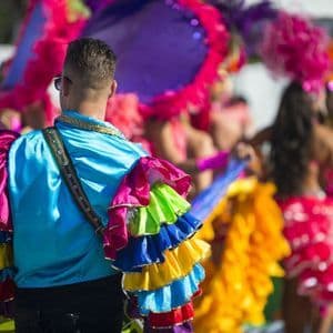 Vista posteriore di un uomo con una camicia blu brillante e maniche a balze colorate, parte di un viaggio di gruppo WeRoad durante una sfilata di carnevale.