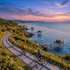Veduta aerea di un gruppo WeRoad in bicicletta su un sentiero costiero verde, con capanne di pescatori sull'acqua al tramonto.