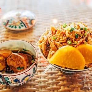 Deux bols de cuisine taïwanaise, l'un avec du poulet effiloché et du radis mariné, et l'autre avec un œuf braisé et du porc, sur une natte tressée.