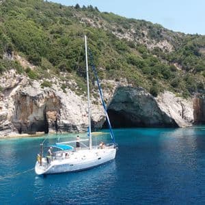 Un voyage de groupe WeRoad en voilier flotte sur des eaux turquoise calmes dans une crique avec des grottes marines et une falaise.