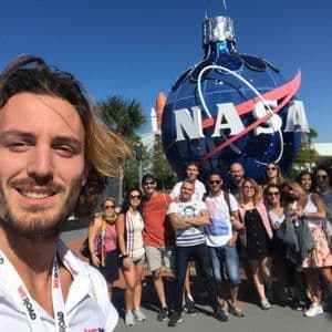 Un grupo de viaje de WeRoad se toma una selfie frente a un gran adorno con el logo azul de la NASA bajo un cielo despejado.