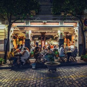 A bustling outdoor restaurant scene at night, with patrons dining at tables along a cobblestone street.