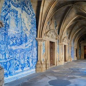 An empty stone hallway with Gothic arches and one wall entirely covered in a blue and white azulejo tile mural.